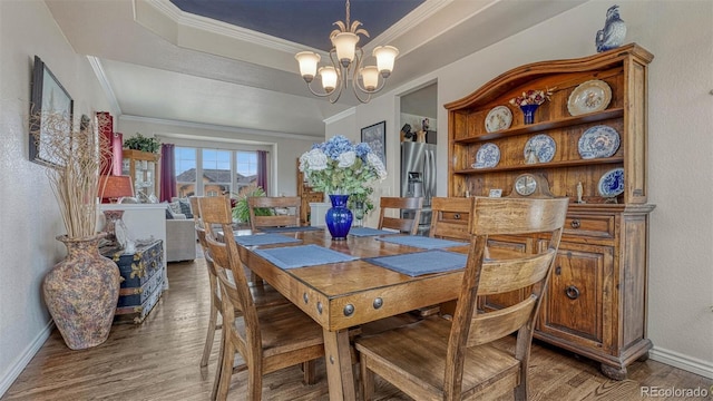 dining room with crown molding, a raised ceiling, a chandelier, baseboards, and wood finished floors