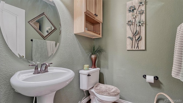 half bath with toilet, a textured wall, and a sink