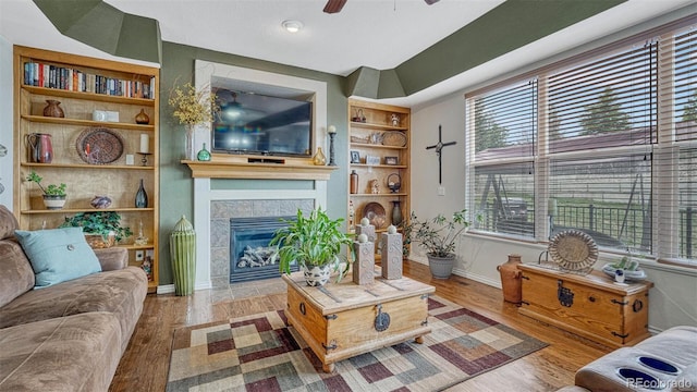 living area with a ceiling fan, built in features, a healthy amount of sunlight, and wood finished floors