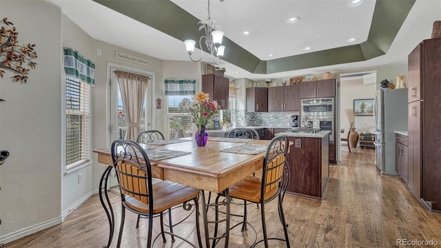dining room featuring baseboards, recessed lighting, a tray ceiling, light wood finished floors, and a notable chandelier