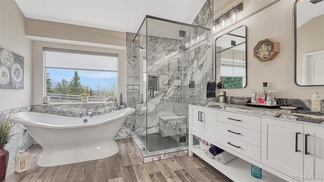 full bathroom with double vanity, a freestanding tub, wood finished floors, a sink, and a marble finish shower