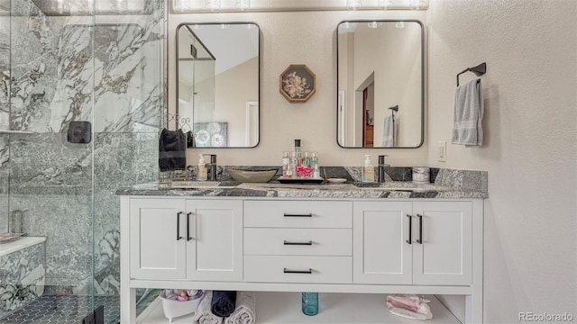 full bath featuring double vanity, a textured wall, and a marble finish shower