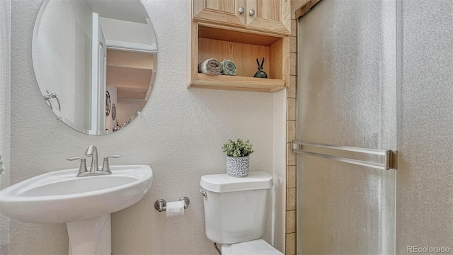 full bathroom with a sink, a textured wall, a shower stall, and toilet