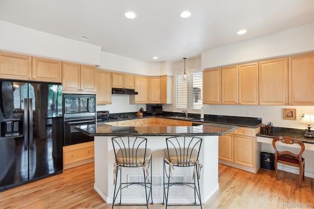 335 Josephine St Unit D, Denver, CO 80206 - kitchen with black appliances, light brown cabinets, under cabinet range hood, light wood finished floors, and a breakfast bar