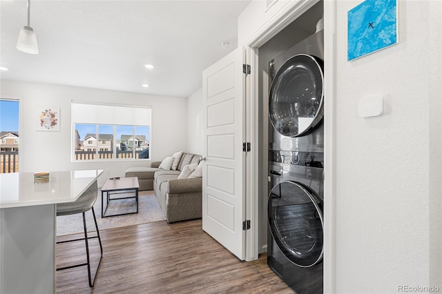 clothes washing area with dark wood-style flooring, a healthy amount of sunlight, stacked washing maching and dryer, and laundry area