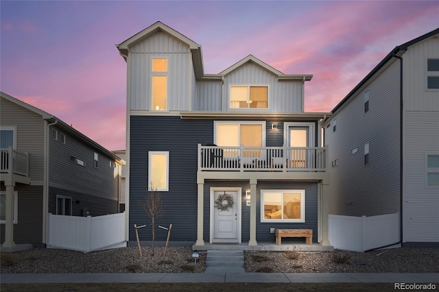 view of front facade with board and batten siding, fence, and a balcony