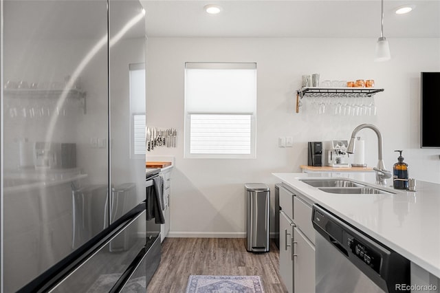 kitchen with stainless steel appliances, light countertops, light wood-style floors, pendant lighting, and a sink