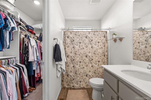 full bathroom featuring a textured ceiling, toilet, a shower with shower curtain, vanity, and a walk in closet