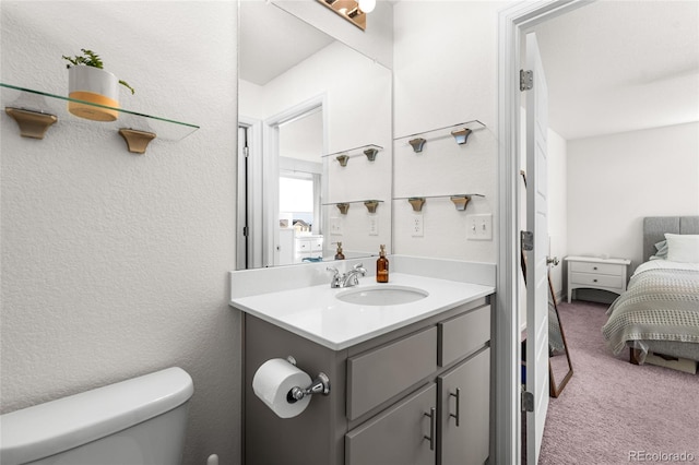 bathroom featuring ensuite bathroom, a textured wall, vanity, and toilet