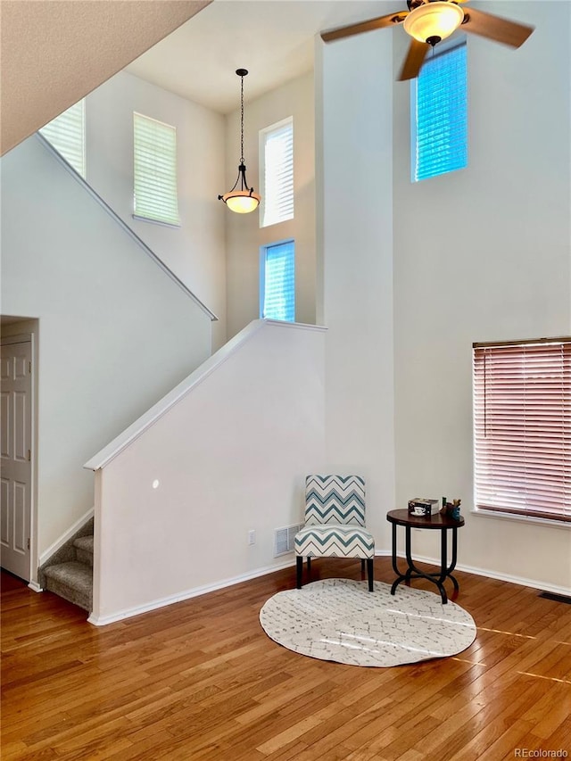 living area featuring visible vents, a high ceiling, wood finished floors, baseboards, and stairs