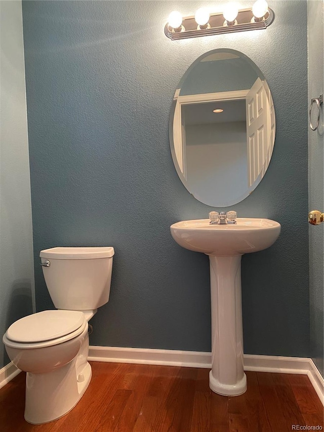 half bathroom with wood finished floors, toilet, and baseboards