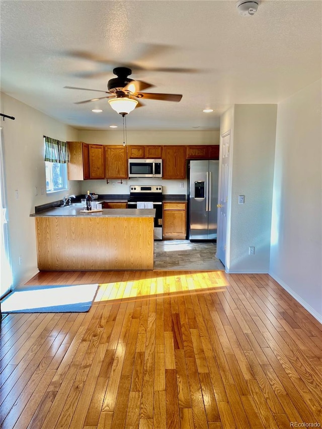 kitchen featuring light hardwood / wood-style floors, kitchen peninsula, a textured ceiling, and appliances with stainless steel finishes