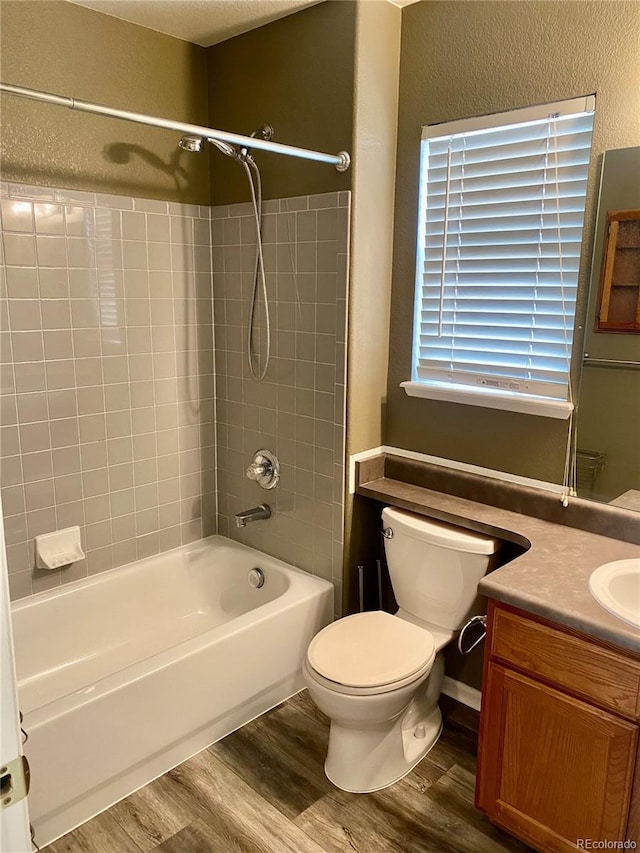 bathroom with a textured wall, toilet, wood finished floors, vanity, and washtub / shower combination