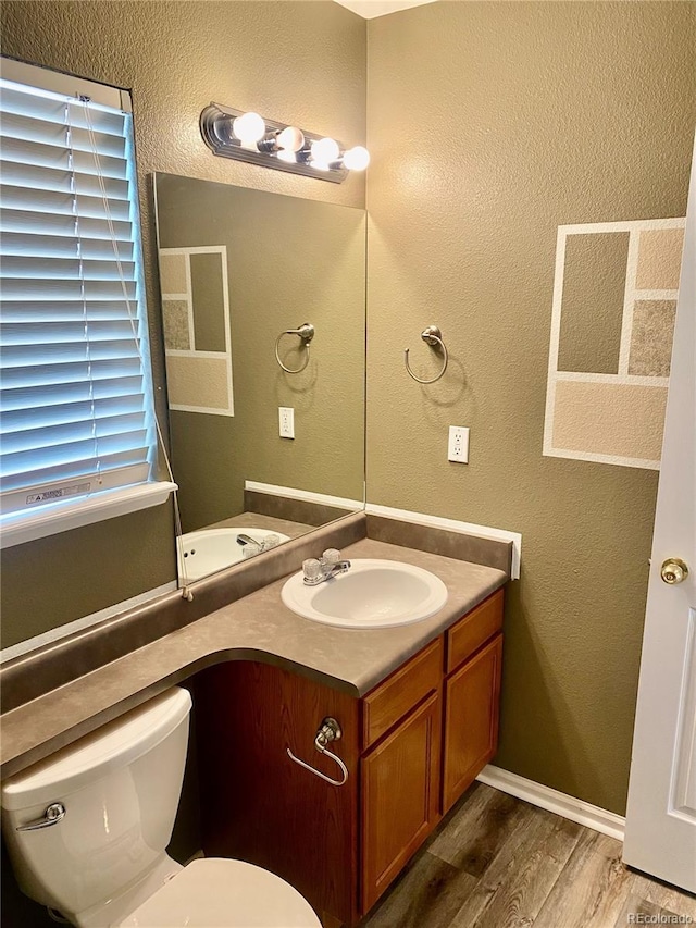 bathroom with toilet, a textured wall, wood finished floors, and vanity