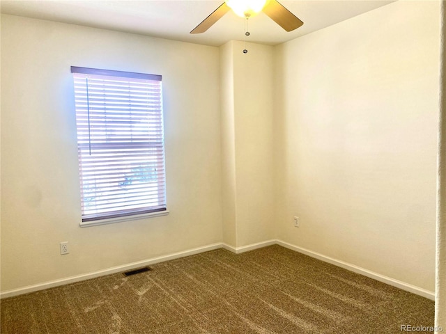 empty room featuring a ceiling fan, visible vents, dark carpet, and baseboards