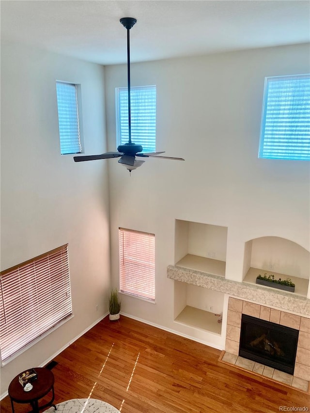 unfurnished living room featuring a tiled fireplace, wood-type flooring, ceiling fan, and built in shelves