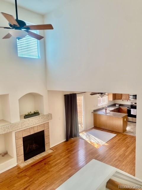 unfurnished living room with a ceiling fan, a fireplace, a towering ceiling, and wood finished floors