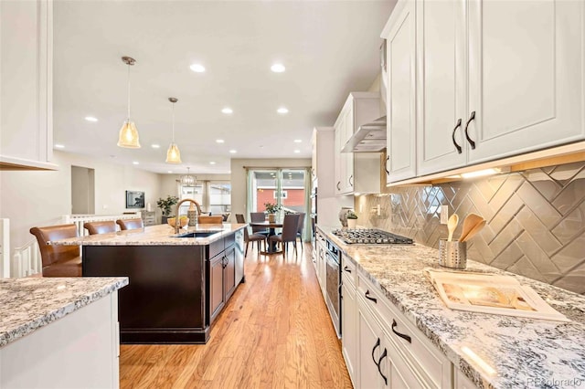 kitchen with a kitchen island with sink, light wood-style flooring, a sink, white cabinets, and stainless steel gas stovetop