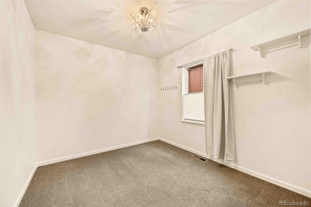 spare room with a notable chandelier, carpet flooring, visible vents, and baseboards