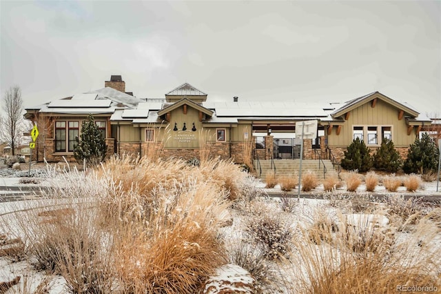 view of front of house with stone siding, roof mounted solar panels, and a chimney