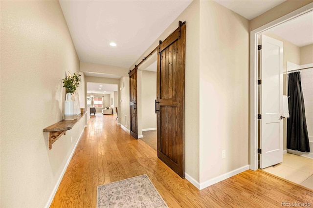 corridor with light wood-type flooring, baseboards, and a barn door