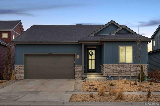 view of front of property featuring stone siding, roof with shingles, driveway, and an attached garage