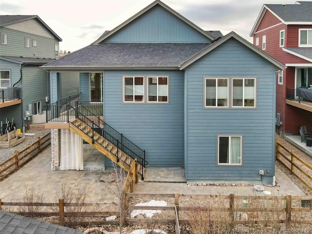 back of property with a shingled roof, stairs, and fence