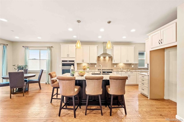 kitchen featuring white cabinets, light wood finished floors, wall chimney exhaust hood, and tasteful backsplash