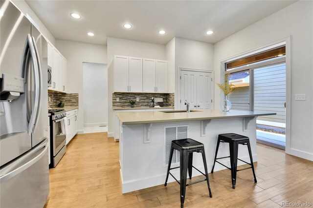 kitchen featuring stainless steel appliances, white cabinets, a center island with sink, and light hardwood / wood-style flooring