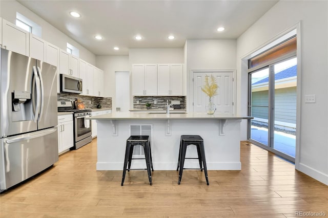 kitchen featuring white cabinets, a center island with sink, appliances with stainless steel finishes, and a kitchen bar