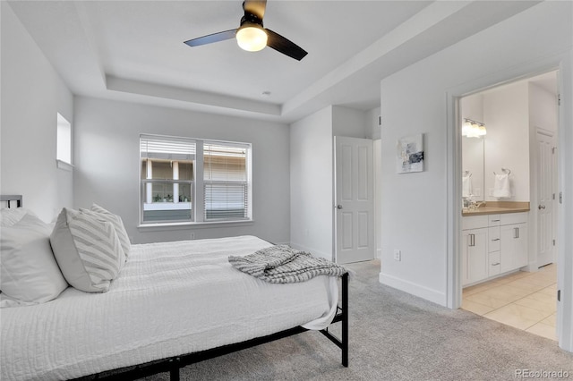 carpeted bedroom with sink, a tray ceiling, connected bathroom, and ceiling fan