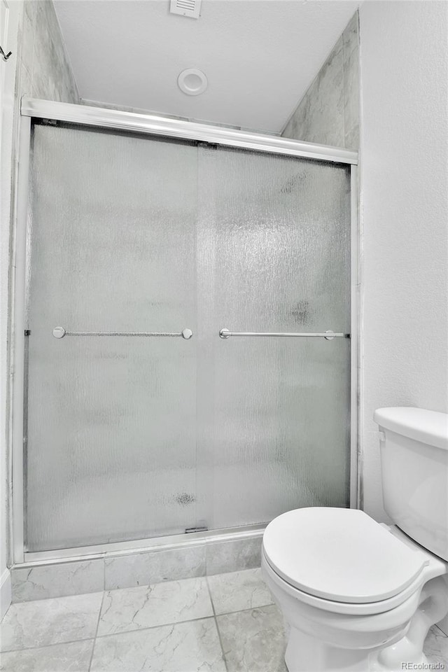 bathroom featuring a shower with door and toilet