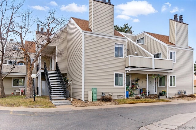 exterior space with a porch, stairway, roof with shingles, a balcony, and a chimney