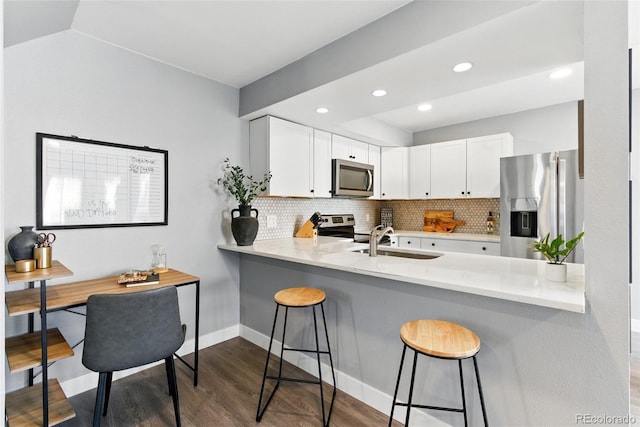 kitchen with dark wood finished floors, a peninsula, a sink, decorative backsplash, and appliances with stainless steel finishes