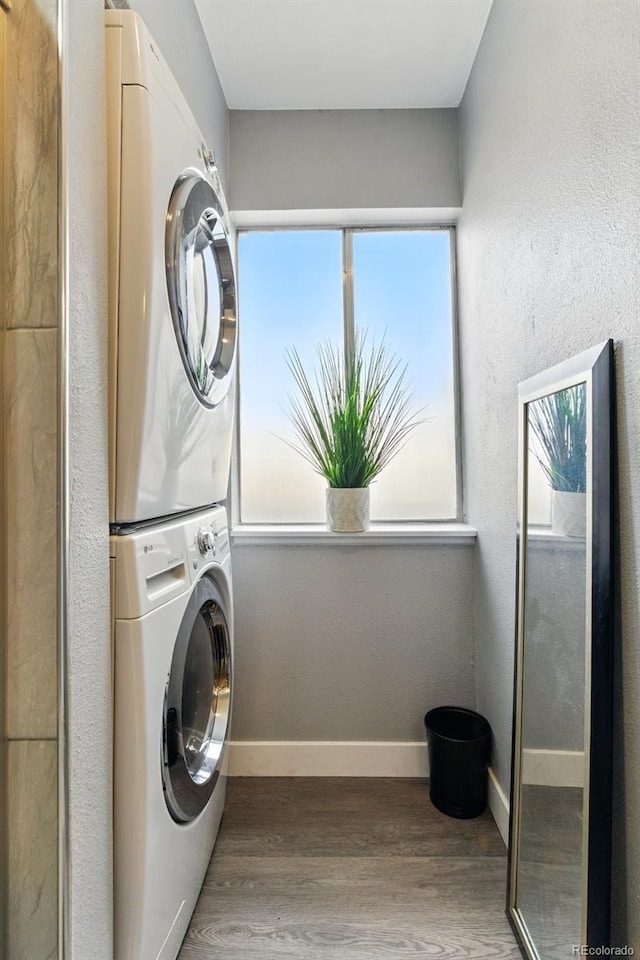 laundry room featuring baseboards, stacked washer and clothes dryer, wood finished floors, and laundry area