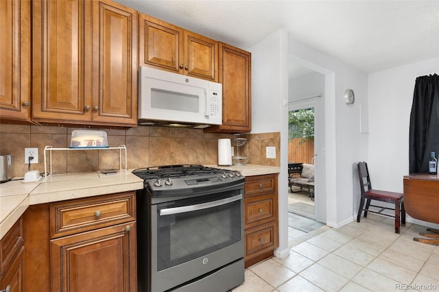 544 S 3rd Ave, Brighton, CO 80601 - kitchen with white microwave, stainless steel gas range, brown cabinets, tasteful backsplash, and light tile patterned floors