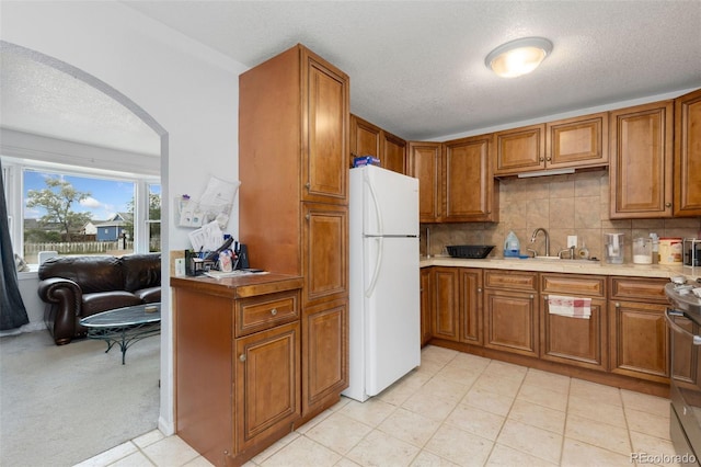 544 S 3rd Ave, Brighton, CO 80601 - kitchen featuring freestanding refrigerator, brown cabinetry, arched walkways, light countertops, and tasteful backsplash