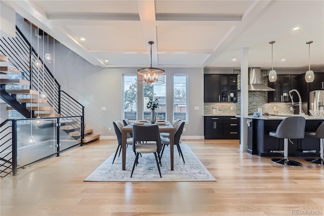 dining space featuring light wood-type flooring, a notable chandelier, coffered ceiling, baseboards, and stairs