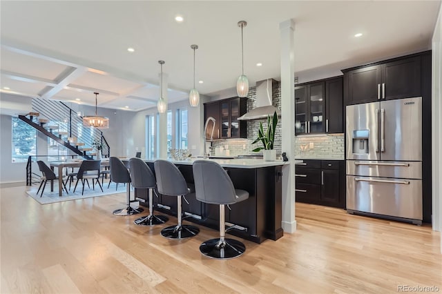 kitchen featuring light wood-style flooring, light countertops, high end refrigerator, wall chimney range hood, and backsplash