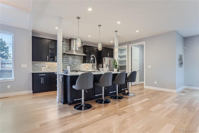 kitchen with dark cabinetry, a breakfast bar, light countertops, wall chimney range hood, and stainless steel fridge