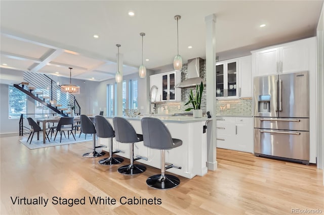 kitchen with wall chimney range hood, coffered ceiling, high quality fridge, white cabinets, and light wood finished floors