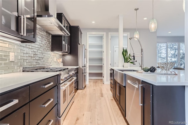 kitchen with light countertops, wall chimney exhaust hood, high quality appliances, and light wood-style flooring