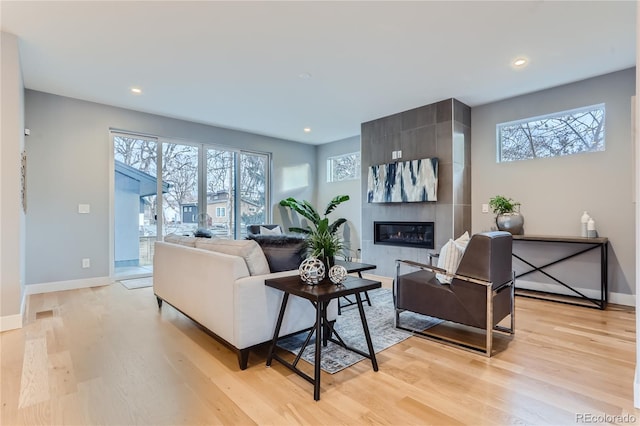 living area featuring baseboards, light wood-style floors, a healthy amount of sunlight, and a tile fireplace