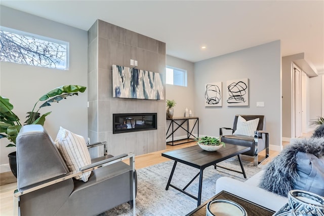 living area with baseboards, a tiled fireplace, and light wood finished floors