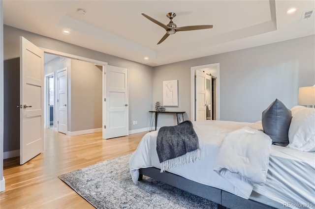 bedroom with visible vents, light wood-style flooring, a raised ceiling, and baseboards