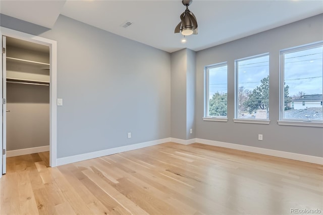 unfurnished bedroom featuring a walk in closet, baseboards, visible vents, and light wood-style flooring