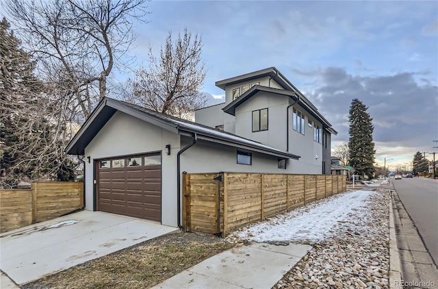 view of side of home featuring concrete driveway, fence, a garage, and stucco siding