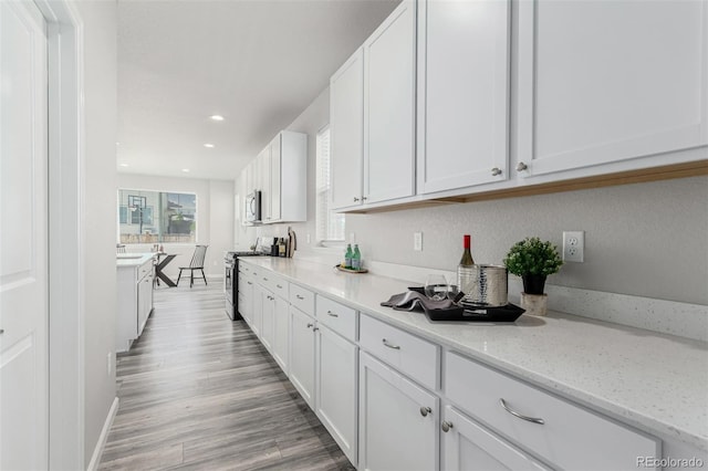 12941 Delaware St, Westminster, CO 80234 - kitchen featuring appliances with stainless steel finishes, white cabinetry, baseboards, light stone countertops, and light wood finished floors