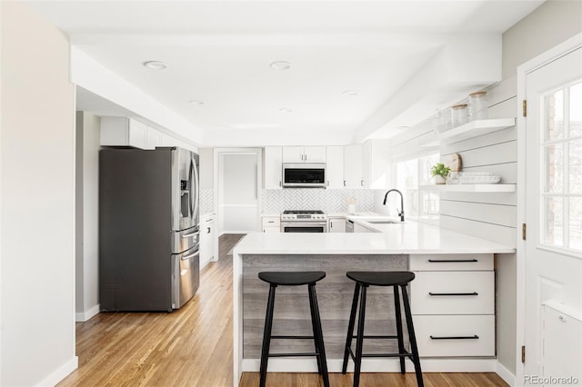 kitchen with open shelves, appliances with stainless steel finishes, a sink, a peninsula, and backsplash