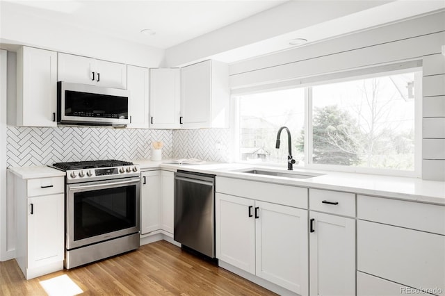 kitchen with white cabinets, a sink, light wood-style flooring, stainless steel appliances, and tasteful backsplash